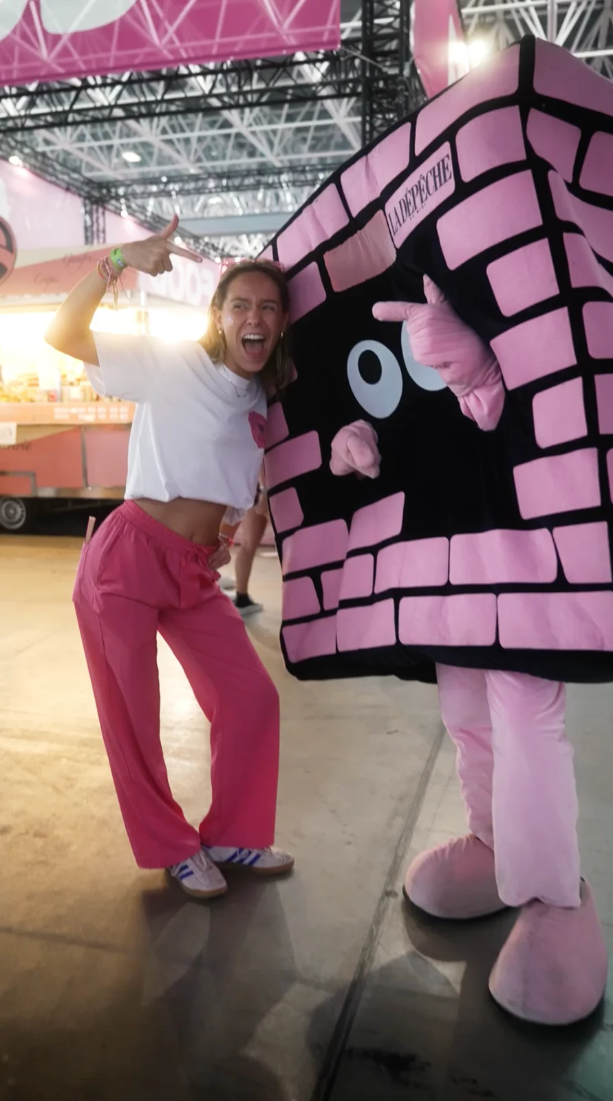 Une personne et une mascotte rose devant un stand événementiel.