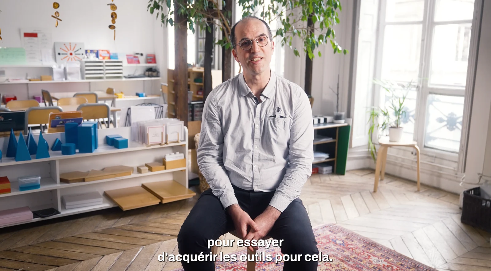 Une personne assise face caméra dans une salle de classe lumineuse.