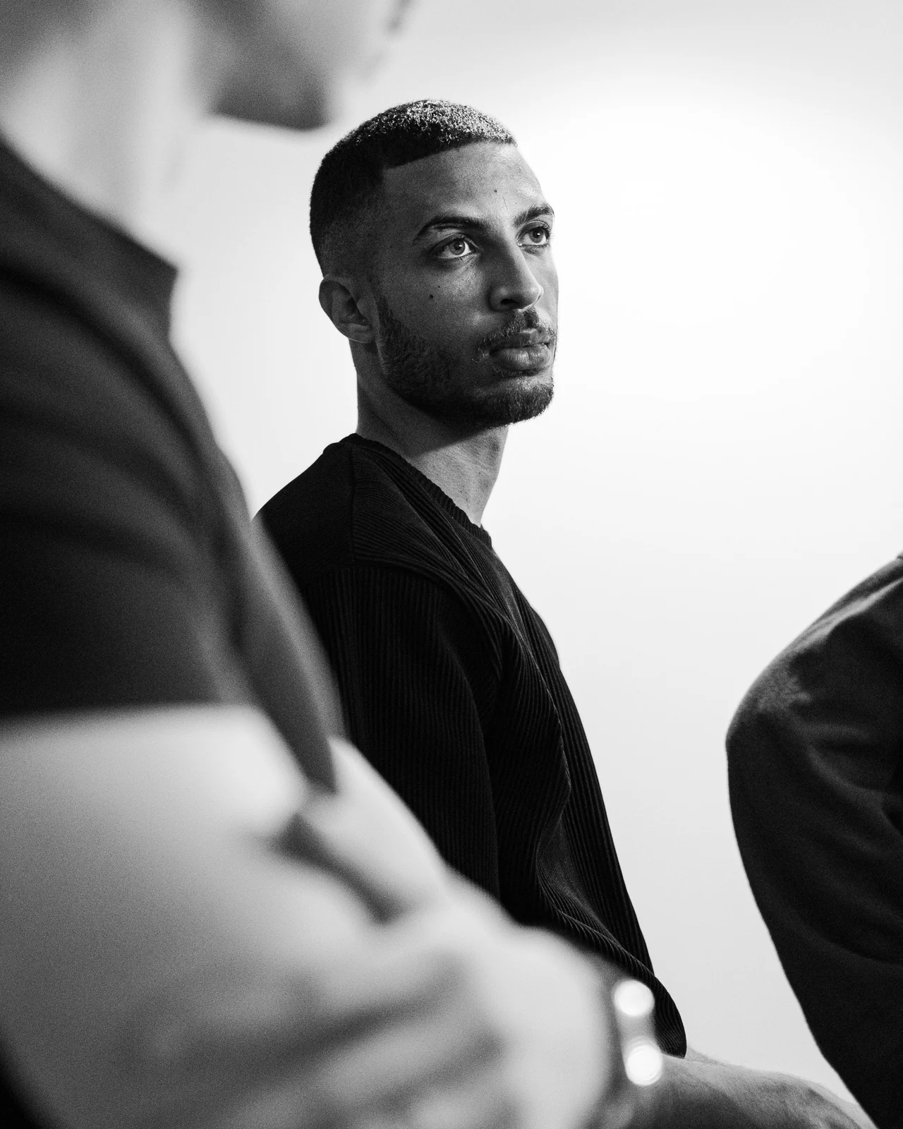 Portrait en noir et blanc, cadré entre deux silhouettes au premier plan.