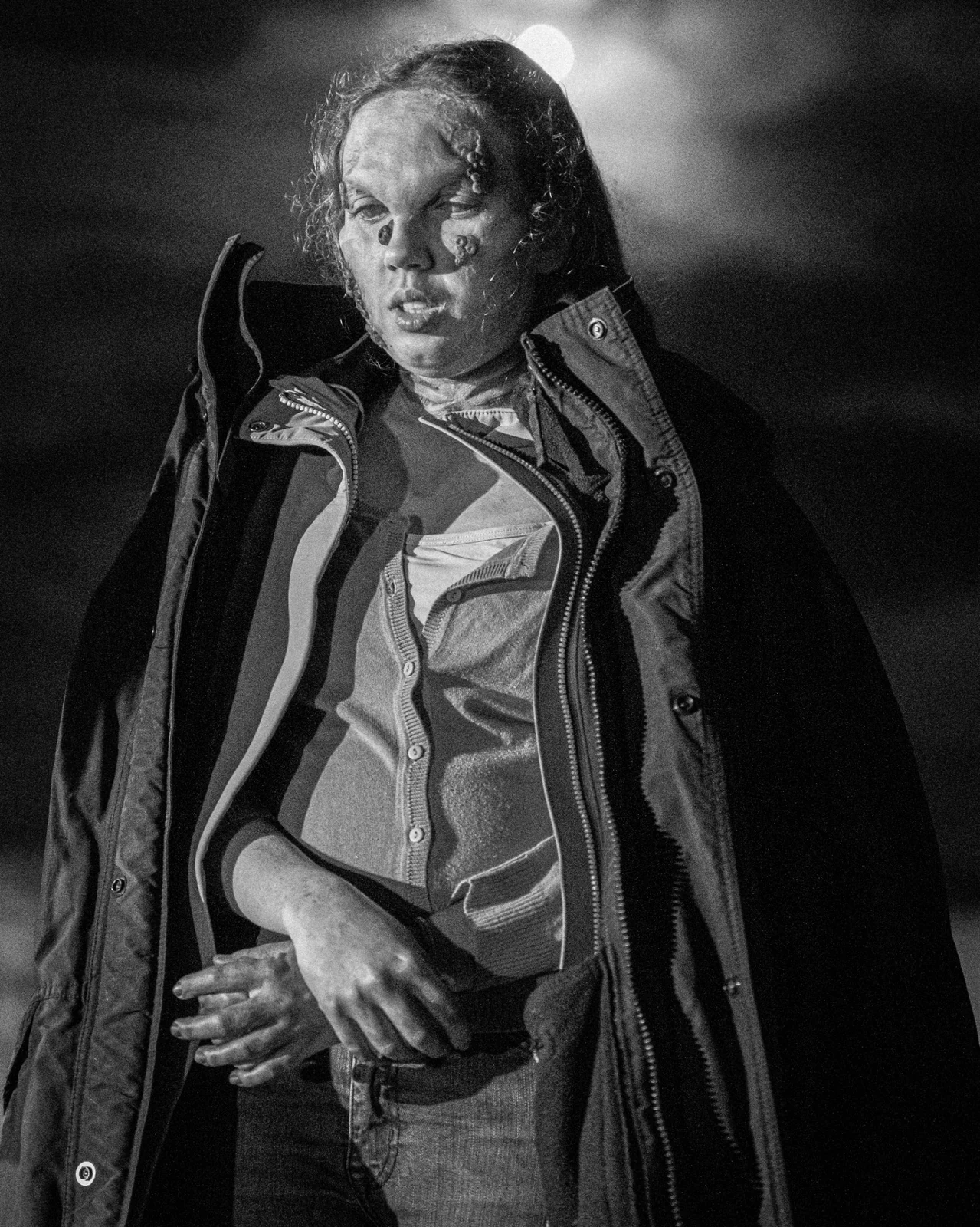 Portrait nocturne en noir et blanc, manteau ouvert et maquillage de tournage.