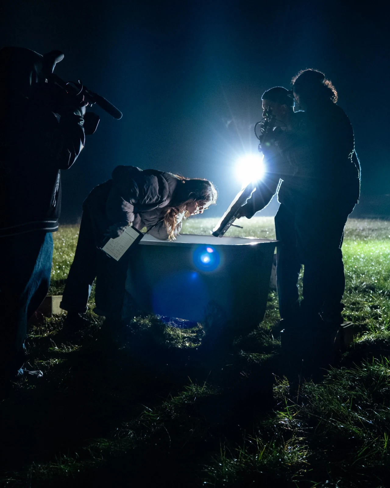 Une équipe réunie autour d’un décor de tournage, éclairée à contre-jour dans la nuit.