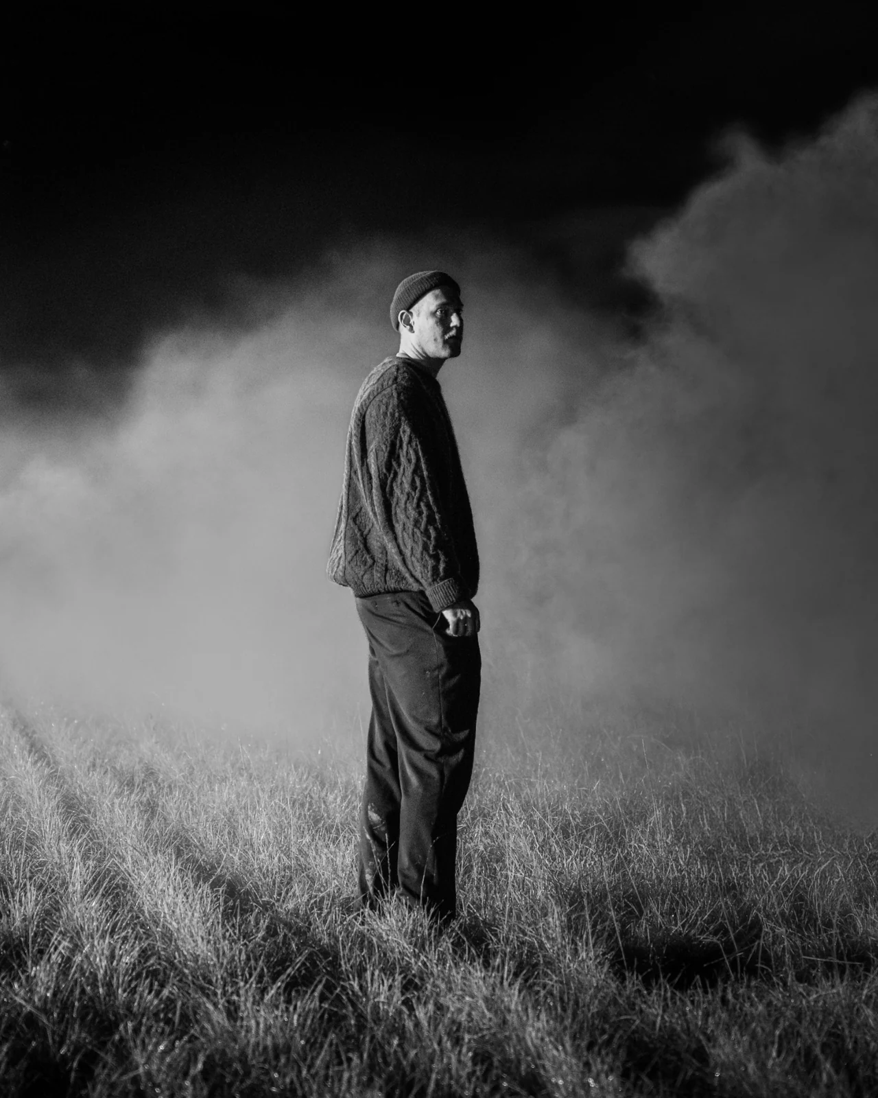 Une silhouette dans un champ de nuit, entourée de brume, en noir et blanc.