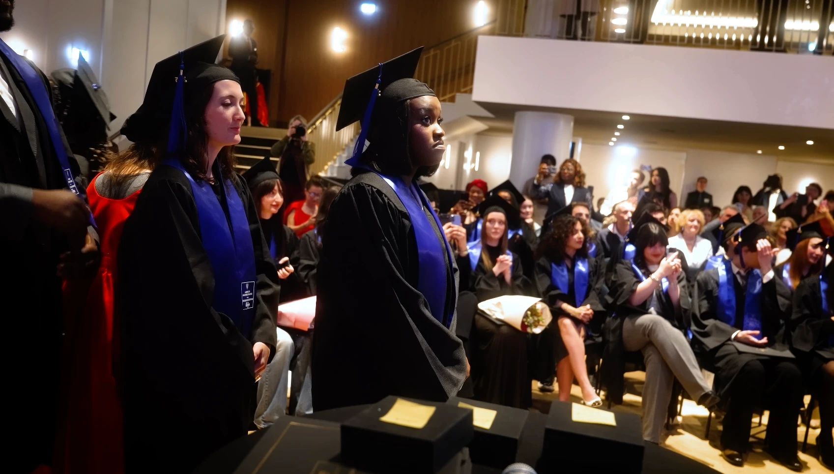 Une personne en tenue de remise de diplômes, entourée de plusieurs personnes.